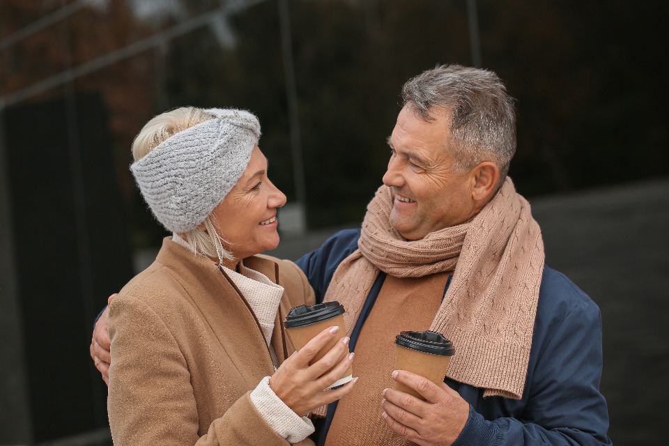 A retired couple laughing together outdoors with takeaway coffee